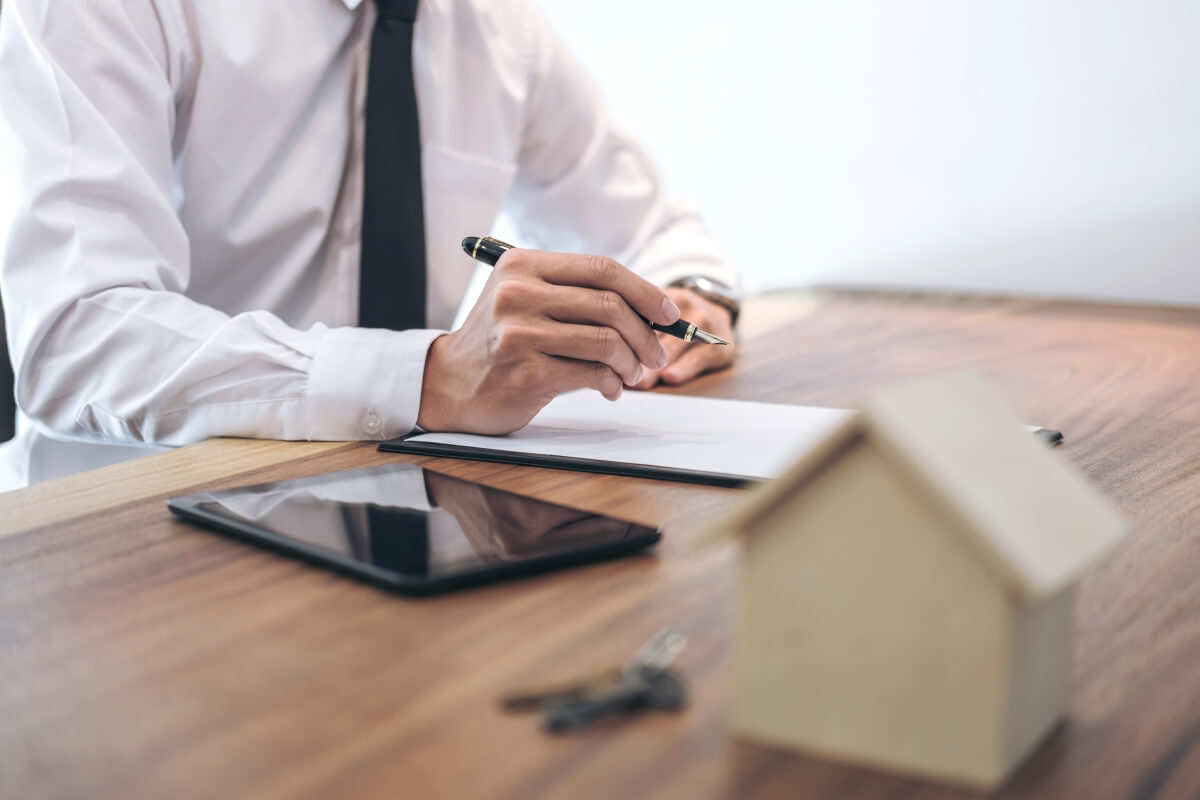Mężczyzna w białej koszuli podpisuje dokumenty dotyczące rozwodów przy biurku, obok klucze i tablet.