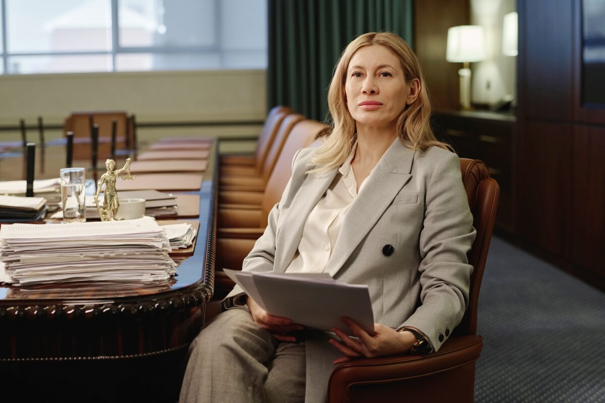 Kobieta w eleganckim garniturze siedzi przy stole z dokumentami, wygląda jak radca prawny.